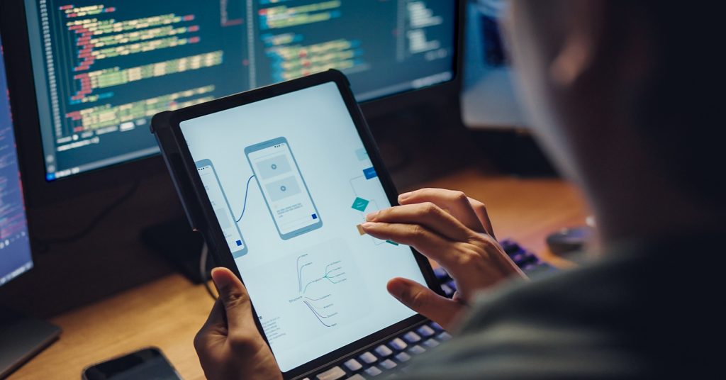 Student working on tablet in front of computer screens.