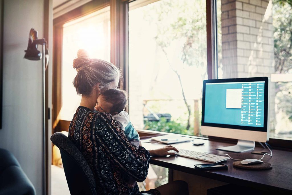 Mother cradling child while working on computer