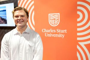 Charles Sturt student Dav Francis standing in front of an orange banner