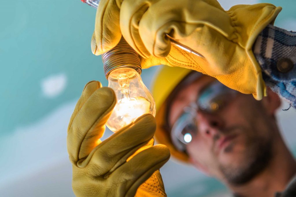 An electrician examines a lit light bulb. Tradie Hamish McCormack made a career change from electrician to lawyer.