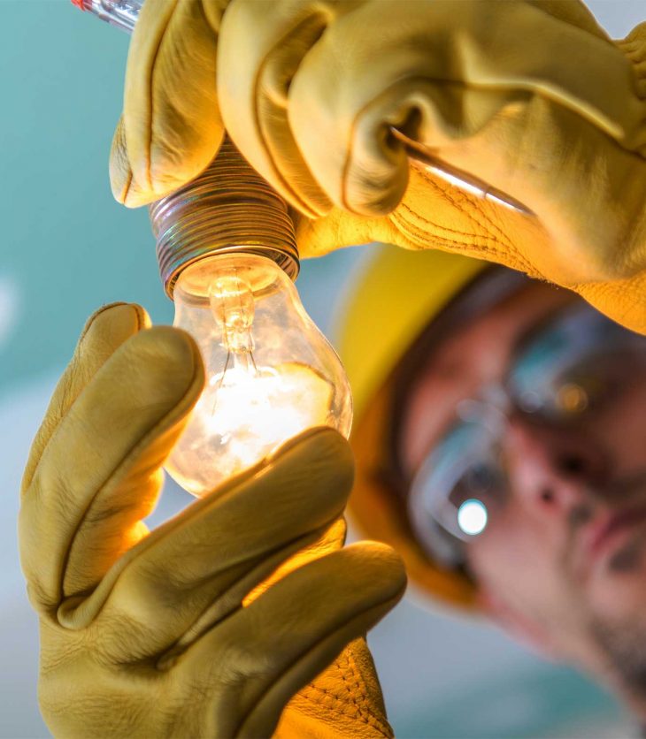 An electrician examines a lit light bulb. Tradie Hamish McCormack made a career change from electrician to lawyer.