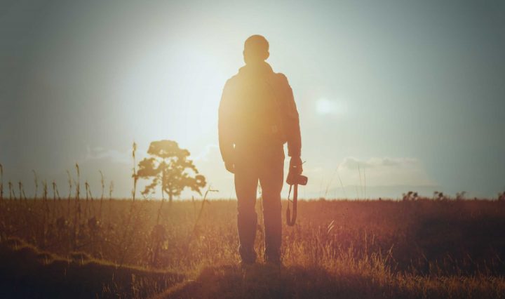 A man is standing in a field, back to the reader. He holds a camera by his side. Its important we develop an understanding of why the arts are important to our regions.