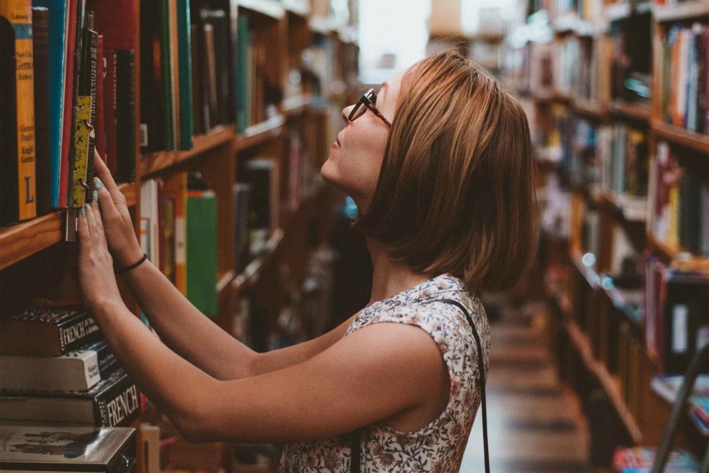 Woman in library looking up at books. Explore information studies at Charles Sturt University and see where it can take you.