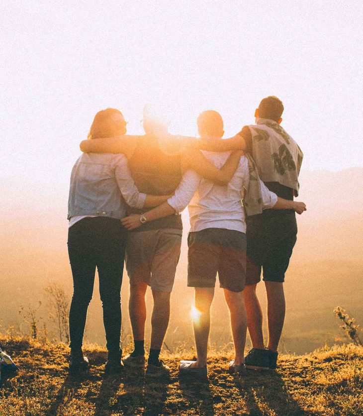Four young people watch the sunrise over the mountains. They may be contemplating six things about uni life they wish they'd known in high school.