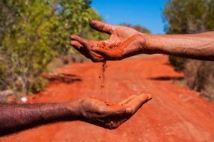 Two hands exchanging red dirt
