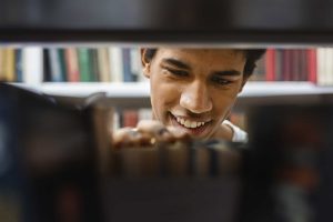 Smiling male student in library looking a text books.