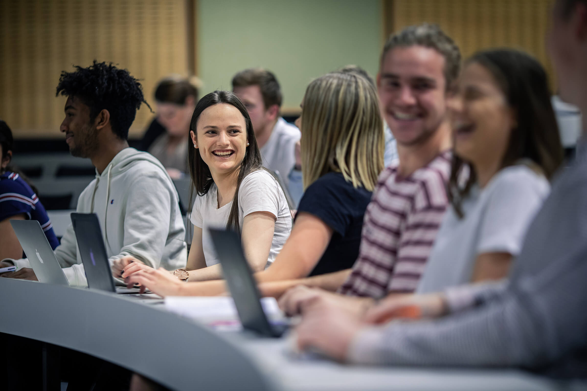 Smiling students working on laptops in a Charles Sturt University lecture room.
