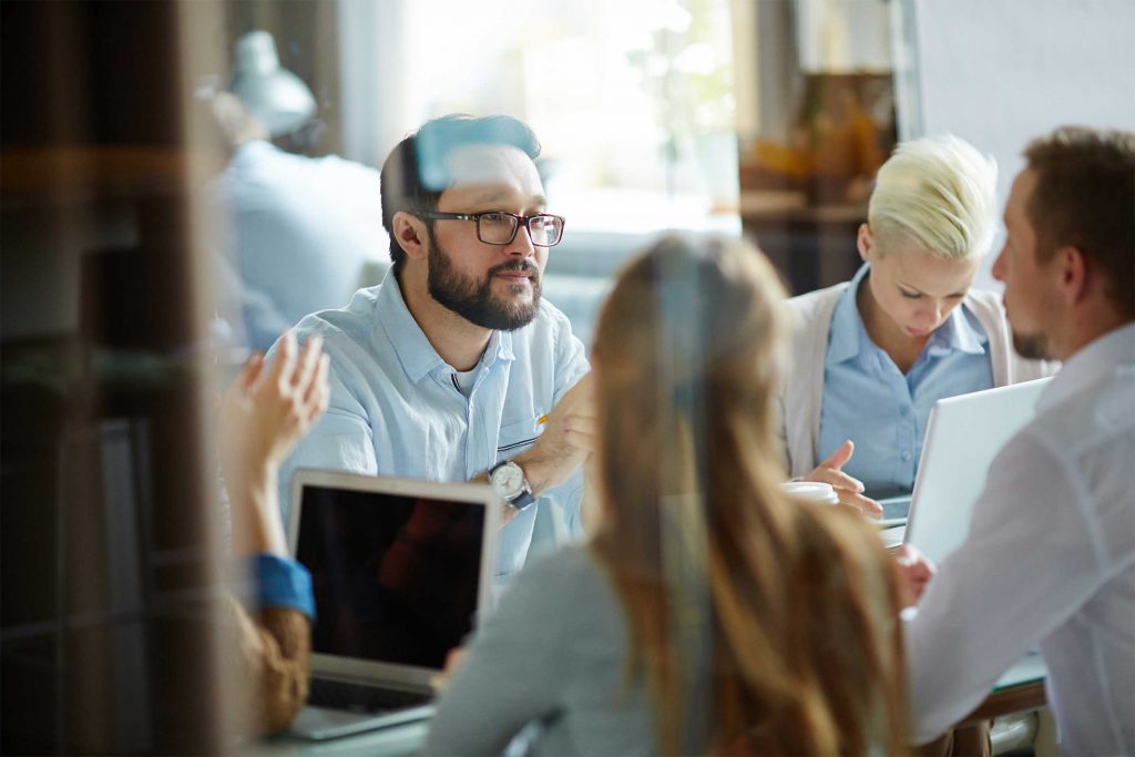 Group of professionals around a table with laptops discussing dealing with a crisis.
