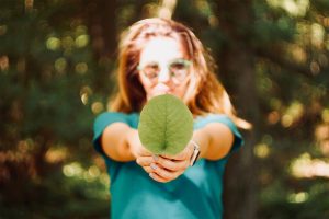 Happy young woman holding broad vibrant green leaf in outstretched arms.