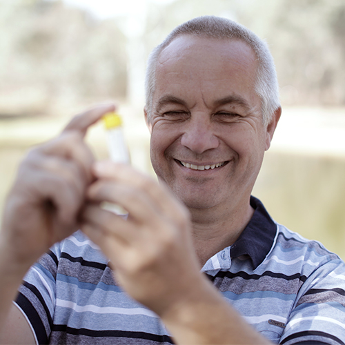 A smiling Dr Jonathon Howard tests water samples from a river.  