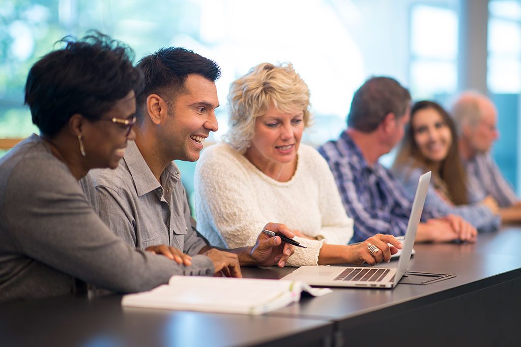 A group of young and mature people helping each other study and using a laptop.