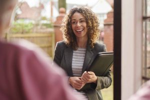 Smiling female social worker with clipboard at the doorstep to a house