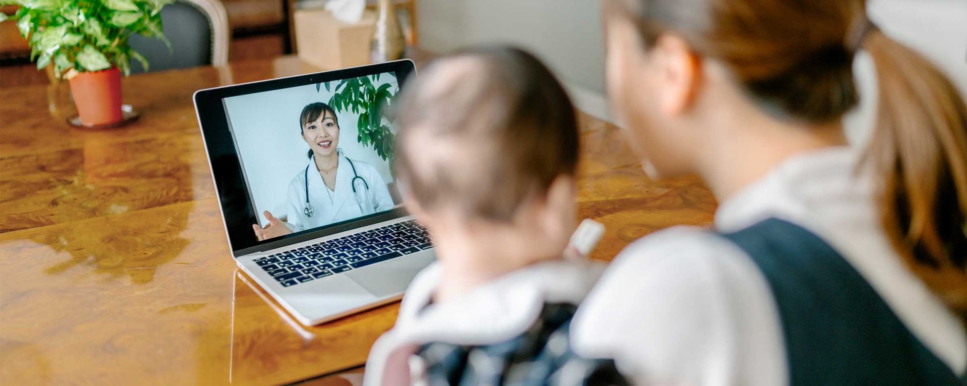 Woman with child speaking to a doctor via a telehealth conference on a laptop