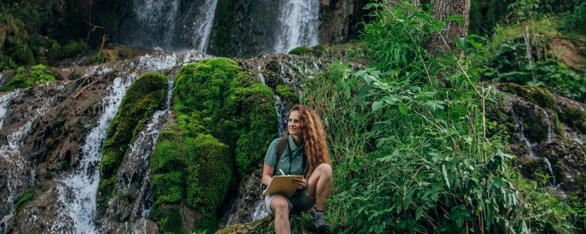 Young woman sitting by waterfall pondering jobs in environmental science