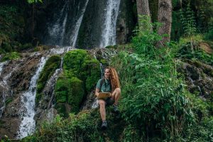 Young woman sitting by waterfall pondering jobs in environmental science