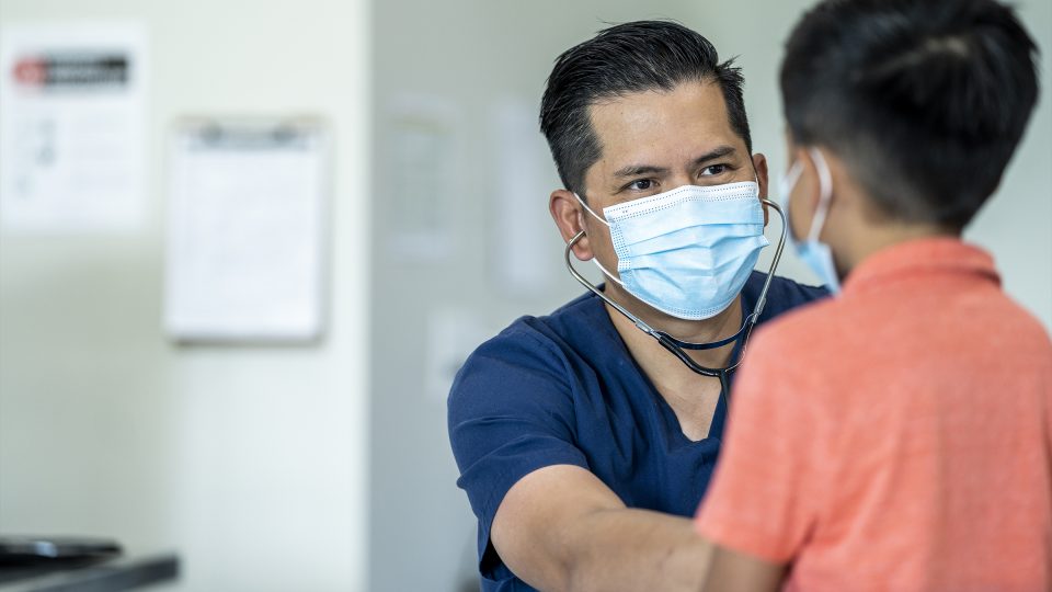 GP treating a child, both wearing face masks