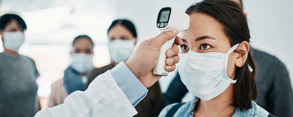 Group of people wearing face masks, one woman getting her temperature checked using a digital thermometer 