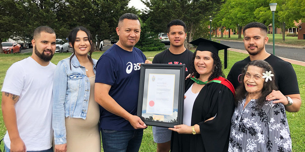 Marion Wichmann with her family holding her certificate in her graduation cap and gown