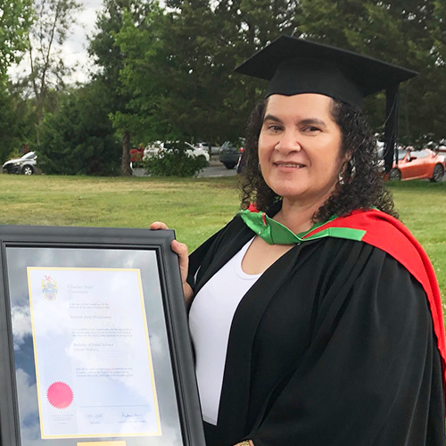 Marion Wichmann holding her certificate in her graduation cap and gown