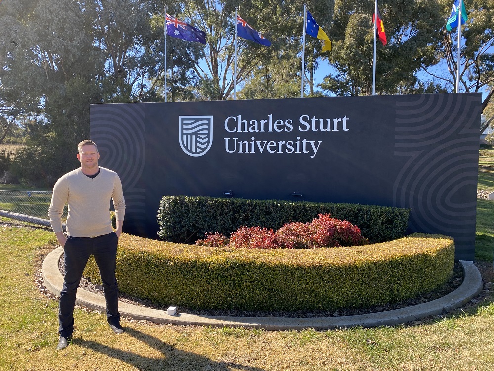 Anthony Vidler, who is studying rural medicine, in front of a Charles Sturt University sign.