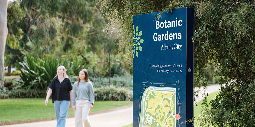 Friends enjoy the Albury Botanic Gardens, walking along a path in front of a map.