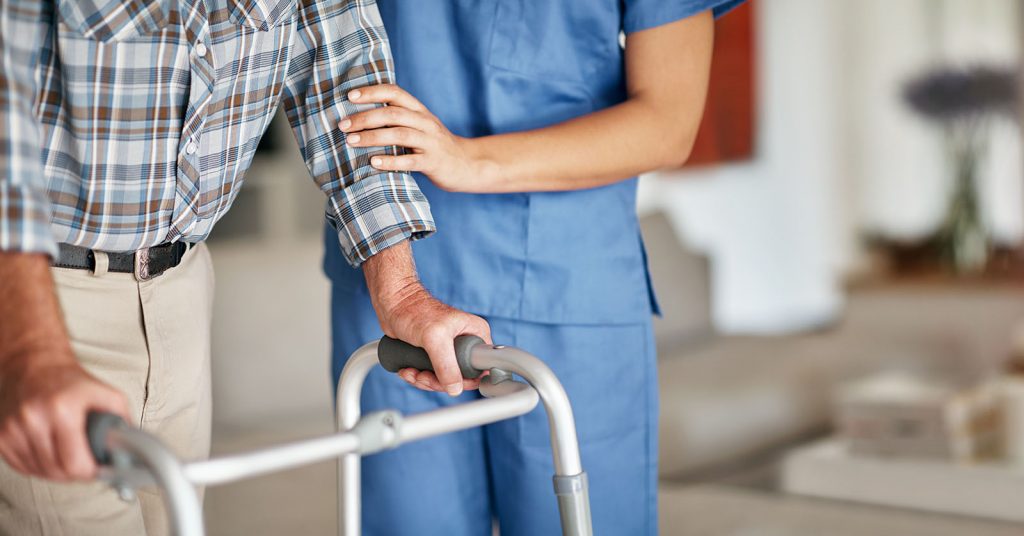 A woman assisting her elderly patient who's using a walker for support