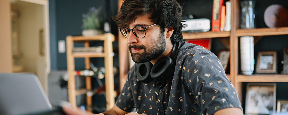 A person sits at a desk with headphones around their neck and works on a laptop.