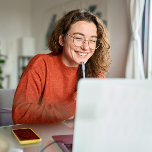 A person sits at a laptop and is smiling at the screen as they are working.