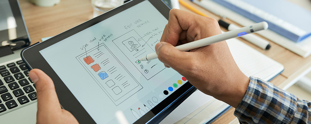 A person is using a tablet to draw a layout for a mobile website using a pencil.