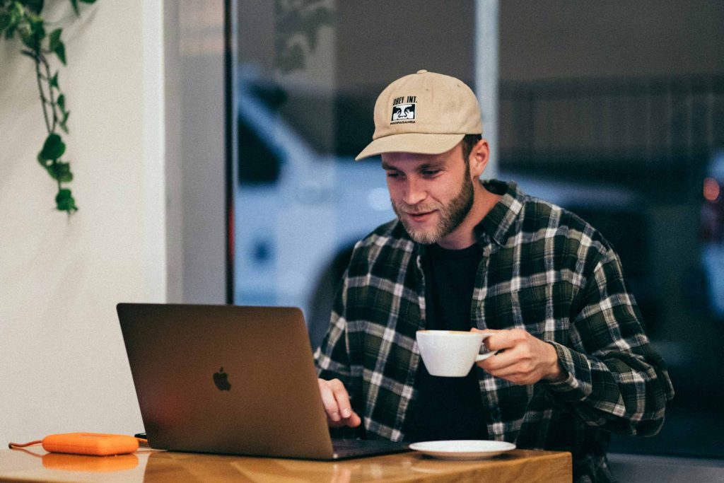 Man with a cup of coffee writing on a laptop