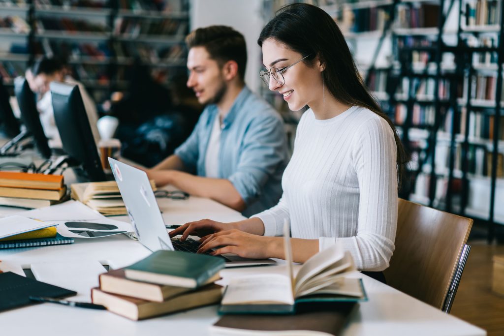 Woman and man writing on laptops surrounded by books