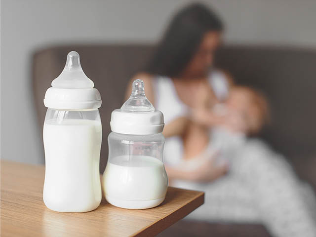 Bottles of baby milk in front of a mother nursing a baby