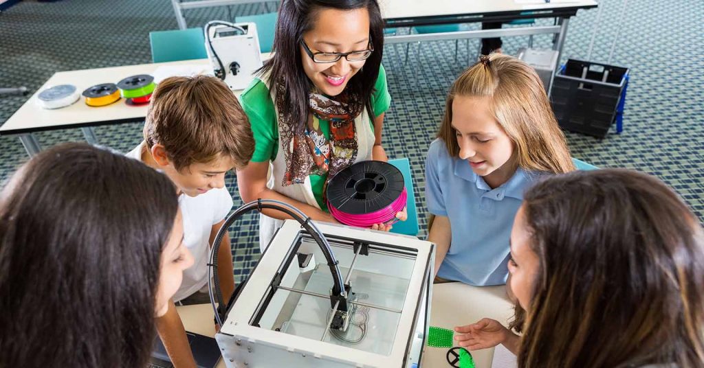 A female teacher helping four students use a 3D printer