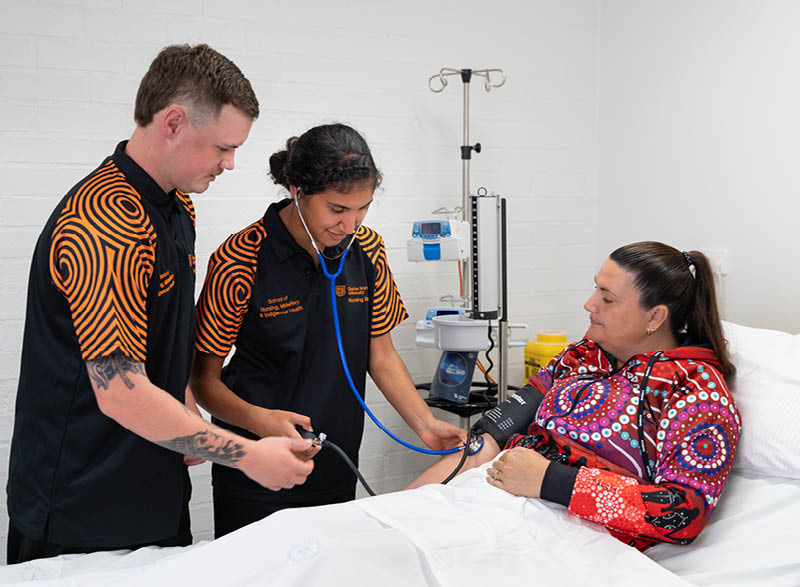 Two student nurses taking a female patient's blood pressure