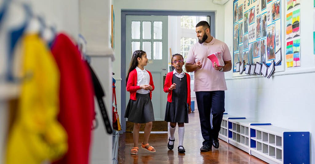 Male kindergarten teacher walking in a school corridor with two students