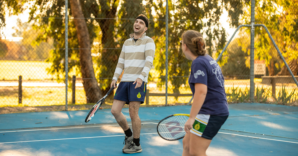 Female and male students playing tennis on campus