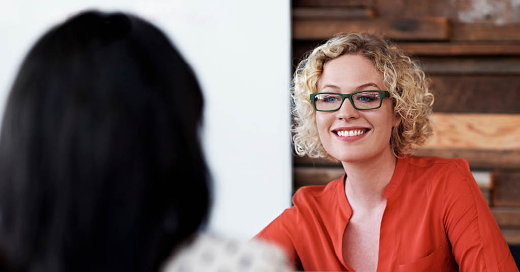 A smiling woman wearing glasses engages in a positive conversation, reflecting approachability and friendly communication.