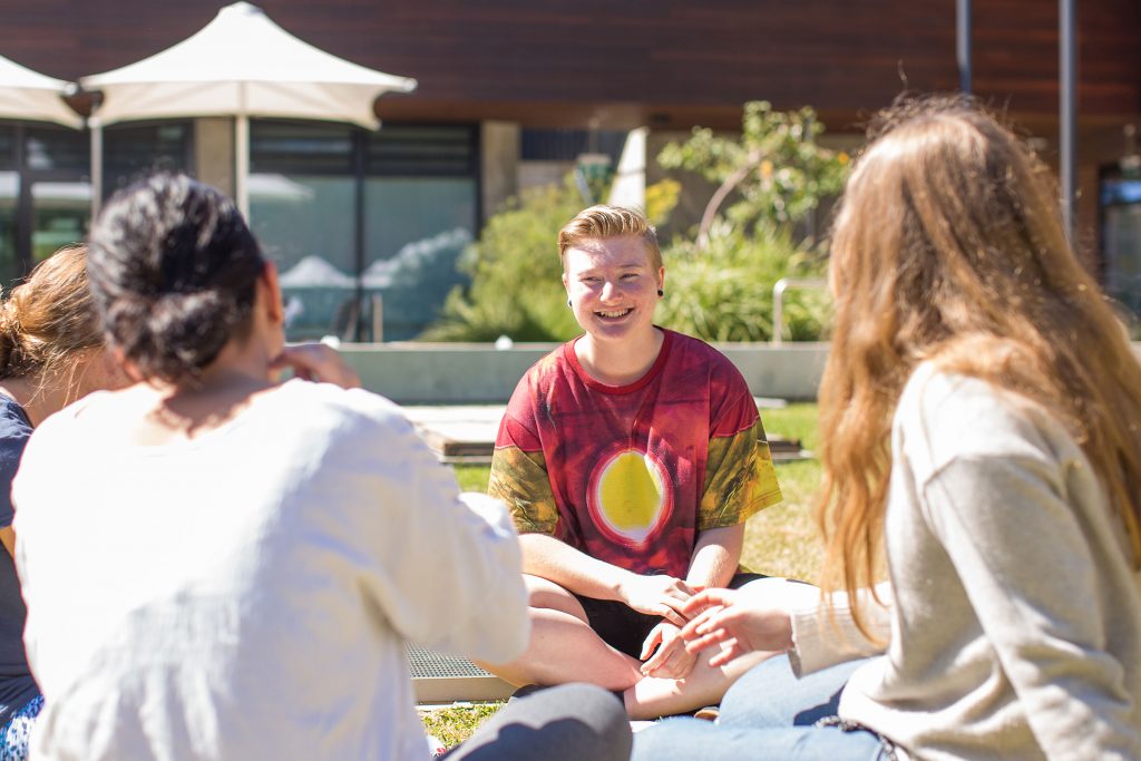 Four people sitting on the grass on a uni campus