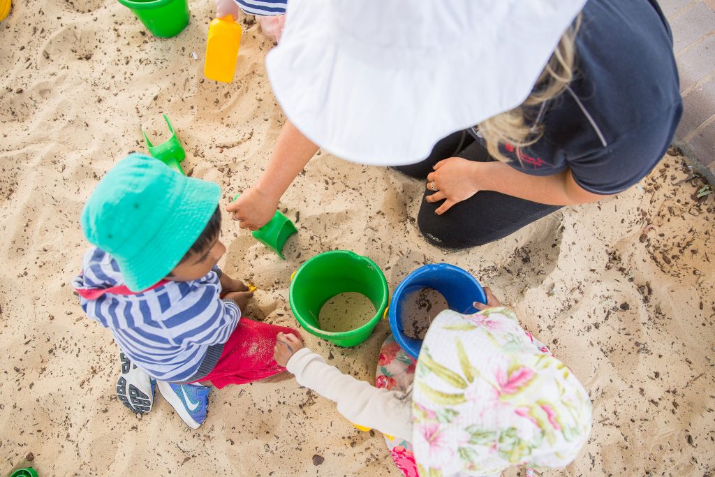 Daycare teacher and child playing in a sandpit