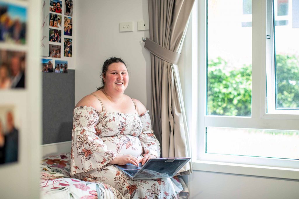 Female student in uni accommodation working at a laptop listing university student essentials