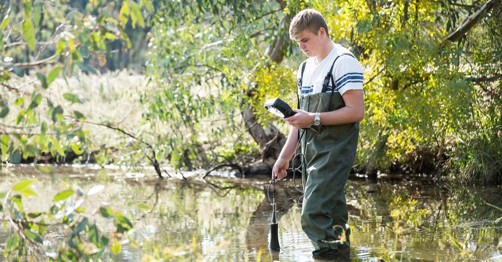 An environmental science student conducting field research in a wetland, taking notes and observing the surrounding water, plants and wildlife.