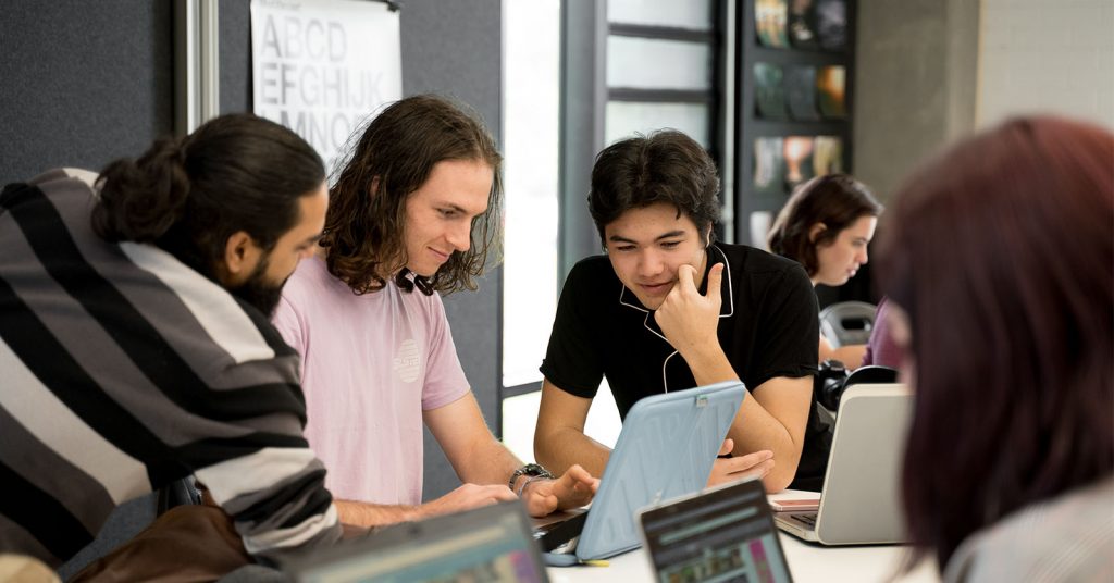 Charles Sturt students studying together around a shared table, laptops and notes open, showing a collaborative and supportive study environment.