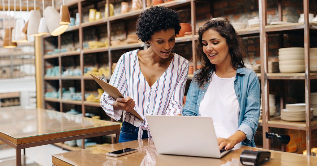 An image of two business owners in what looks like a pottery or home goods store looking at their laptop and clipboard