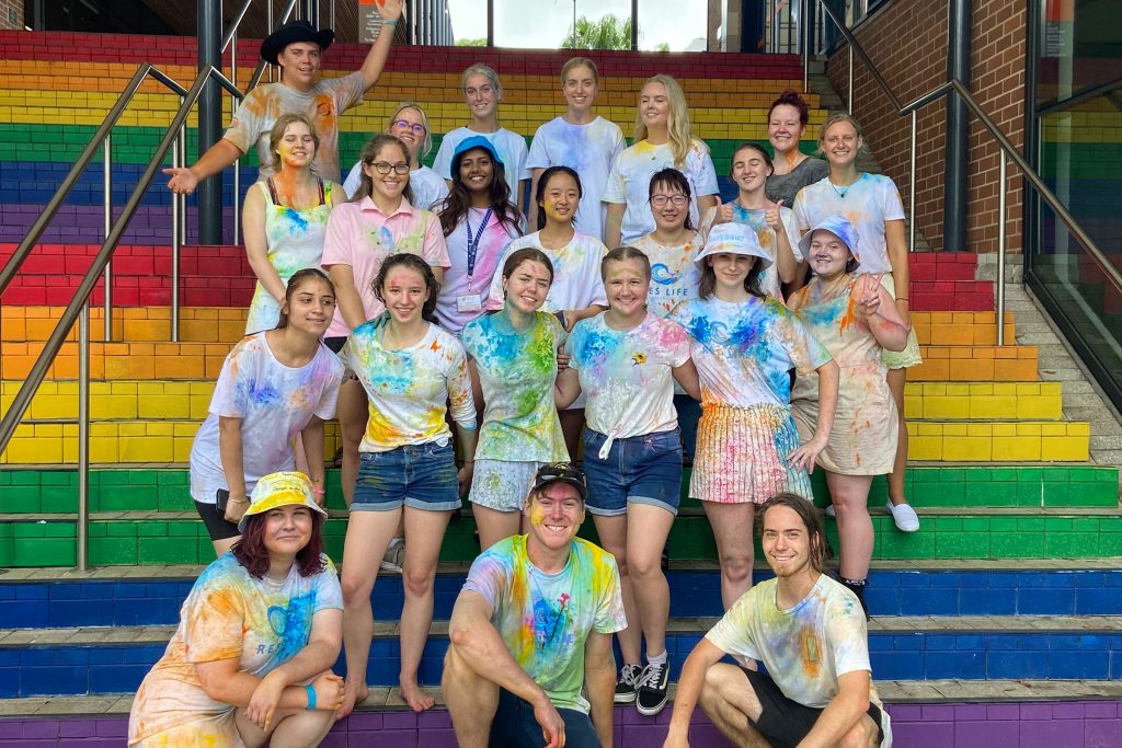 University students all smiling on the rainbow-colored steps.