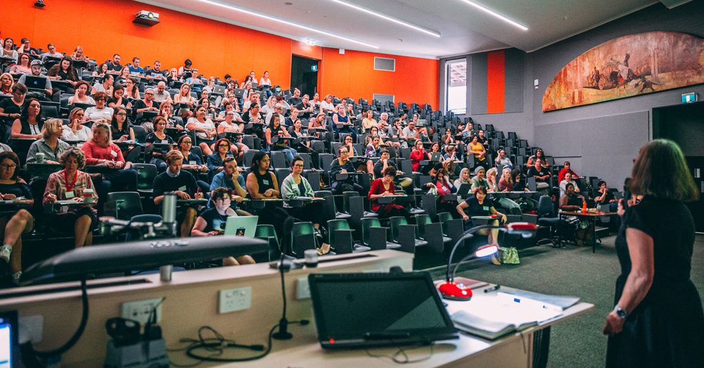 Lecturer delivering a lesson to a theatre full of students.
