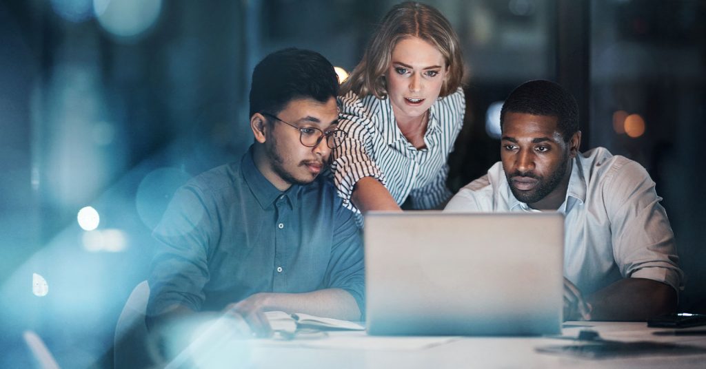Three digital health professionals sit together at a desk, leaning in toward a laptop and discussing the information on screen.