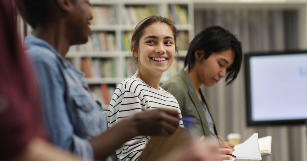 Woman smiling at a a friend in a lecture, holding a notepad