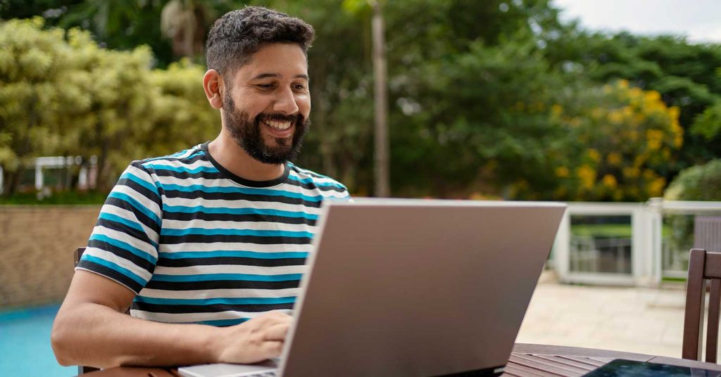 A man in striped tshirt smiles at a laptop
