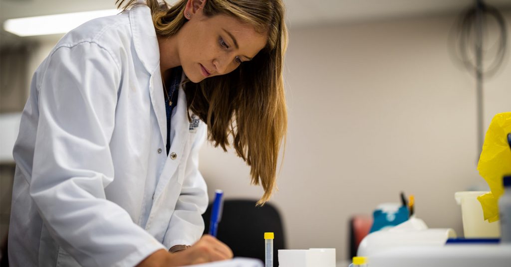 Female research scientist wearing laboratory coat analysing an experiment at a bench. Close up shot of a woman shown standing