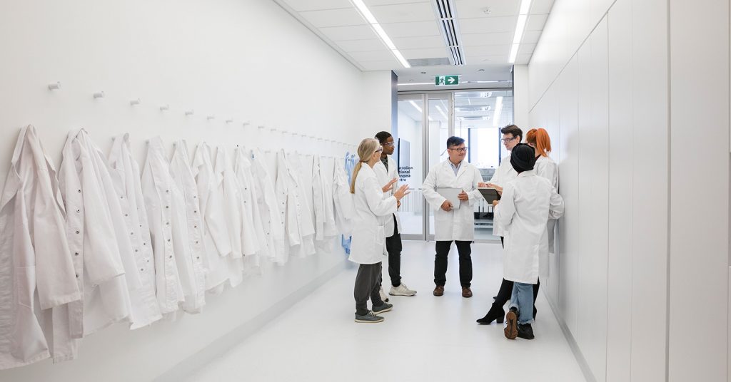 Medical protective clothing hanging in a hallway. A team of pharmacy students gather around talking